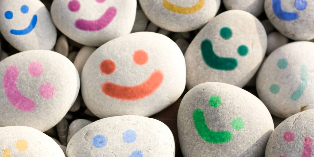 mehrere graue Kieselsteine mit bunten Lach-Gesichtern bemalt, Stein-Smileys