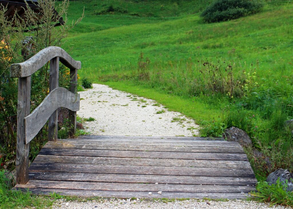 Übergang, Holzbrücke über Bach heller geschwungener Kiesweg führt durch grüne Wiese