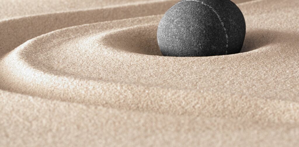Zen Garten. Weißer Sand mit eingeritzter Welle, heller und dunkler rundlicher Stein ähnlich Yin-Yang-Zeichen